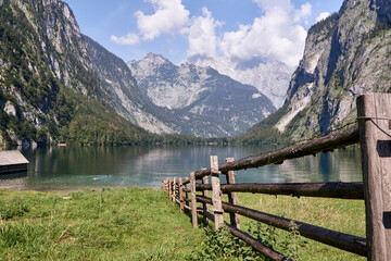 Wooden fence leads to lake Obersee in front of idyllic mountain landscape in Schönau, Bavaria, Germany.