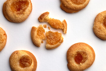Five handmade cookies with apricot jam arranged in even rows from an angle. One in the center is broken. on white background
