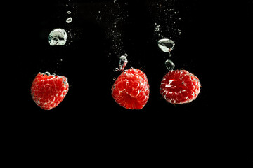 Raspberries splashing into clear water isolated on black background.