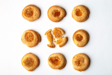 Nine handmade cookies with apricot jam arranged in even rows. One in the central row is broken. on white background