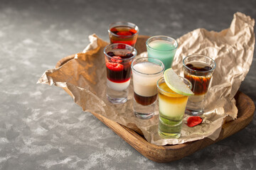 Various alcoholic shots in shot glasses on serving tray on grey background