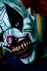 scary evil clown with a big knife in his mouth