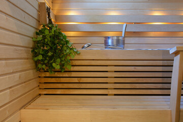Modern wooden Finnish sauna interior with fresh birch whisk, bucket and ladle to throw water on the...