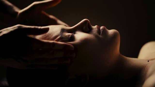 Young woman has facial massage. Authentic footage of luxury spa treatment. Warm colors, charming light. Slow motion.