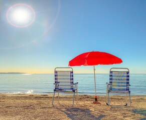 Two deckchairs under a red parasol on the beach, Cannes.