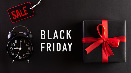 Top view of Black Friday Sale text with black gift box and alarm clock on black background. Shopping concept boxing day and black Friday composition.