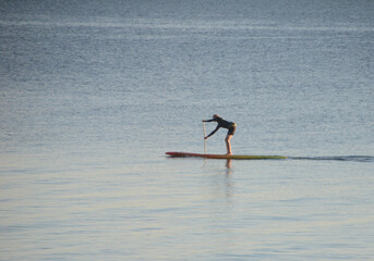 Calm sea with a person rowing a surfboard.