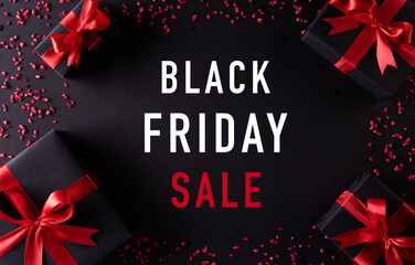 Top view of black christmas gift boxes with red ribbon on black background with text Bkack Friday...