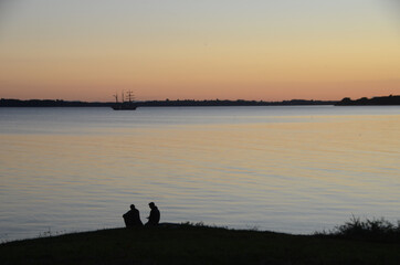 Old sail ship passes out on the sea while two persons in silhouette watch