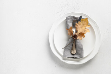 Fall table setting with autumn leaves and white plate on white table. Top view. Copy space.
