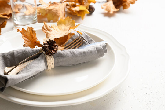 Fall table setting with autumn leaves and white plate on white table. Close up.