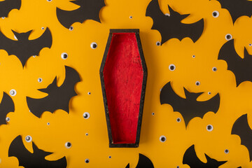 A Halloween yellow background with many plastic eyes, bats and an open black and red coffin in the center. Festive flat lay. A place for your product.