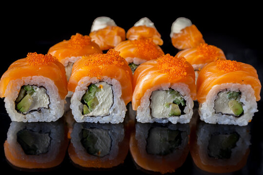 Salmon sushi set. Sushi roll Philadelphia with red fish, salmon, red caviar. Roll with soft avocado and cream cheese under a layer of massago caviar. Classic sushi on a black background. Food.