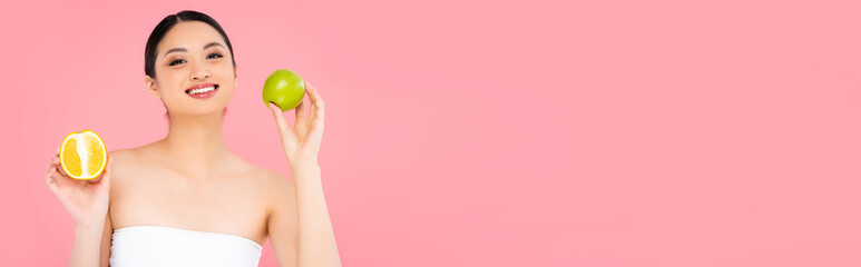 Obraz na płótnie Canvas panoramic concept of asian woman holding whole apple and half of juicy orange isolated on pink