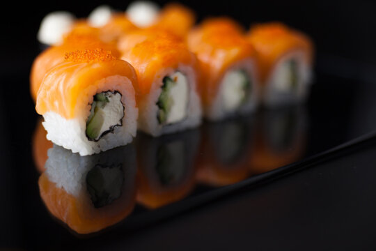 Salmon sushi set. Sushi roll Philadelphia with red fish, salmon, red caviar. Roll with soft avocado and cream cheese under a layer of massago caviar. Classic sushi on a black background. Food.