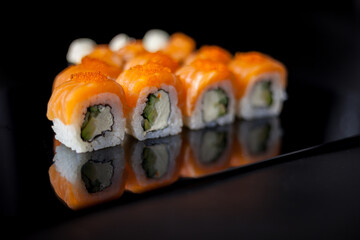 Salmon sushi set. Sushi roll Philadelphia with red fish, salmon, red caviar. Roll with soft avocado and cream cheese under a layer of massago caviar. Classic sushi on a black background. Food.