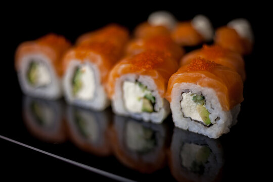 Salmon sushi set. Sushi roll Philadelphia with red fish, salmon, red caviar. Roll with soft avocado and cream cheese under a layer of massago caviar. Classic sushi on a black background. Food.