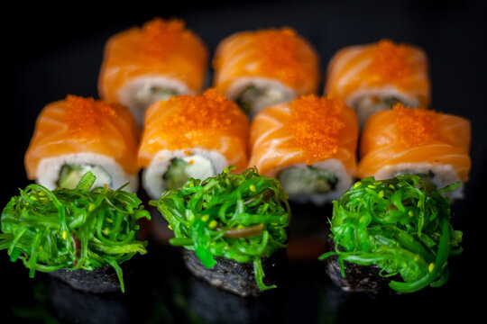Salmon sushi set. Sushi roll Philadelphia with red fish, salmon, red caviar. Roll with soft avocado and cream cheese under a layer of massago caviar. Classic sushi on a black background. Food.