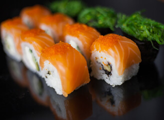 Salmon sushi set. Sushi roll Philadelphia with red fish, salmon, red caviar. Roll with soft avocado and cream cheese under a layer of massago caviar. Classic sushi on a black background. Food.