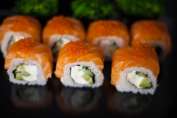 Salmon sushi set. Sushi roll Philadelphia with red fish, salmon, red caviar. Roll with soft avocado and cream cheese under a layer of massago caviar. Classic sushi on a black background. Food.