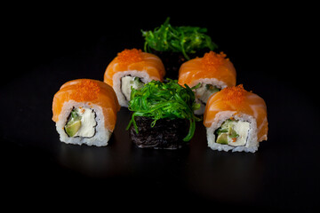 Salmon sushi set. Sushi roll Philadelphia with red fish, salmon, red caviar. Roll with soft avocado and cream cheese under a layer of massago caviar. Classic sushi on a black background. Food.