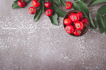 Ripe red cherries in a ceramic bowl with leaves on stone background
