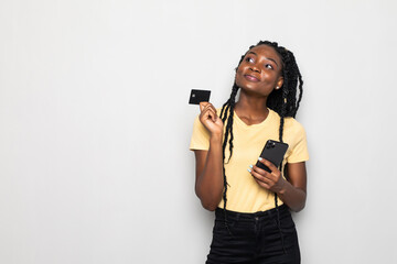 Smiling happy cheerful young woman using mobile phone holding credit card posing isolated over white wall background