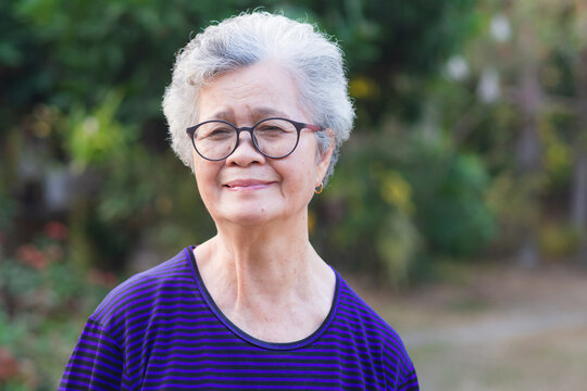 An elderly Asian woman smiling and looking at camera while standing in a garden