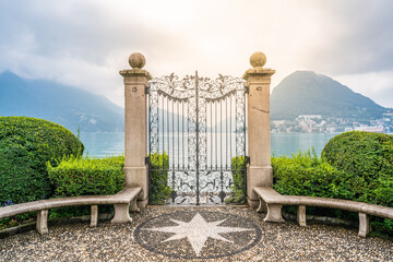 Old wrought-iron gate on Lake Lugano banks in Parco Civico Ciani public garden and dramatic light...