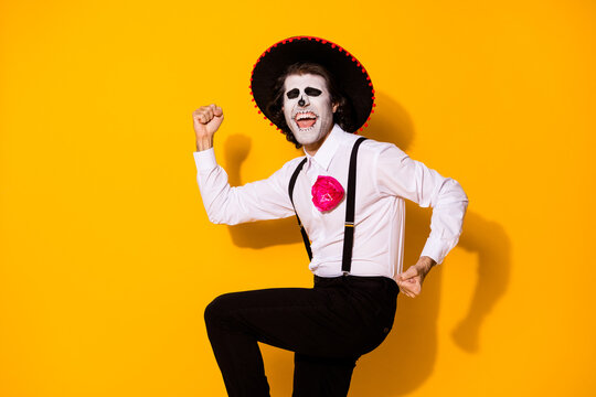 Photo of scary crazy evil creature guy raise fists close eyes open mouth successful cemetery raid wear white shirt death costume sugar skull suspenders isolated yellow color background