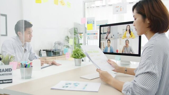 Asia businesspeople using desktop talk to colleagues discussing business brainstorm about plan in video call meeting in new normal office. Lifestyle social distancing and work after corona virus.