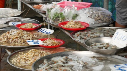 Marine products on sale in local market. From above fresh fragrant seafood in ice with price on shelves on market. Crabs squids shrimps and raw lobsters in basins with water and price tags.