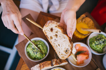 Close up view of female hands grease guacamole sauce on fresh homemade bread during healthy breakfast, selective focus on fresh vitamin ingredients mixed in mexican puree for organic nutrition lunch