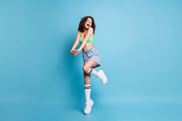 Fototapeta na wymiar Full body photo of crazy fanatic lady model chilling party concert vacation close eyes raised knee tiptoe slim belly yell sing wear green top jeans skirt isolated pastel blue color background