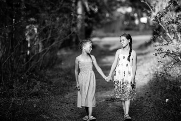 Fototapeta premium Two girlfriends ten-year-old girls walk in the alley. Black and white photo.