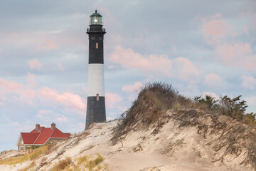 The Fire Island Lighthouse during a beautiful sunset filled with colorful clouds and sand dunes....