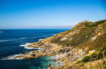Fototapeta premium Photo of some rocks and a lighthouse in Galicia, Spain during summer holidays. Blue ocean, empty beach.