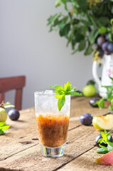 Cold refreshing autumn plum mousse, plum smoothie with ice and mint in a glass on a wooden table, leaves in a vase, morning in the village, rustic concept