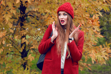 Happy  blonde woman in red hat and jacket posing in autumn park.