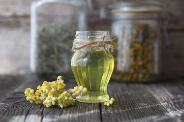 Beautiful glass bottle of essential oil and dried immartelle flowers on a wooden background.