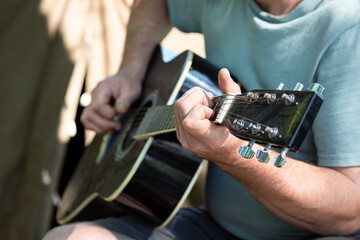 Man playing guitar sitting near tent outdoors. Closeup of hands. Camping, touristic life, romance. Selective focus. Summer vacation concept.