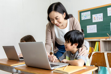An Asian female teacher teaches primary school students to use computers and tablets to search for...