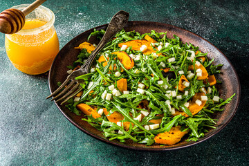 Homemade pumpkin salad with grilled pumpkin slices, arugula and cheese. Autumn pumpkin salad recipe, dark background copy space