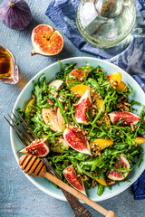 Autumn fig and arugula salad recipe. Whole vegan paleo fruit and vegetable fall salad idea. Homemade salad bowl with figs, arugula, peach and apple slices, nuts and honey. Blue concrete background cop