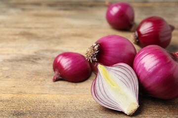 Ripe red onion bulbs on wooden table, closeup