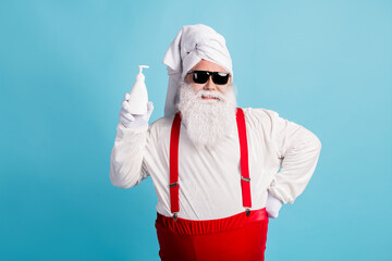 Photo of pensioner old fat man grey beard hold soap antiseptic bottle prepare wash hand contact people wear santa x-mas costume towel turban suspender sunglass isolated blue color background