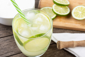 Brazilian lemon caipirinha in a glass with ice with fruit slices over wooden board