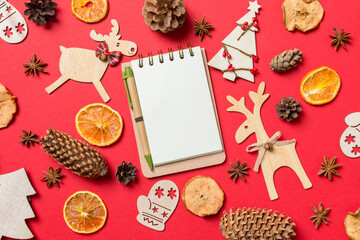 Top view of notebook, red background decorated with festive toys and Christmas symbols reindeers and New Year trees. Holiday concept