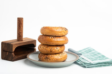 A Single Tall Stack Of Freshly Baked Bagels On A Ceramic Plate With Wood Cutting Stand And Knife