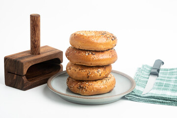 A Single Tall Stack Of Freshly Baked Bagels On A Ceramic Plate With Wood Cutting Stand And Knife
